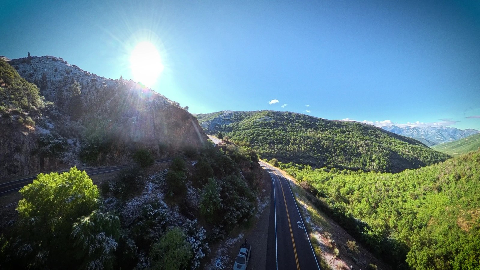 Aerial view of a motorcycle road winding through a green canyon at golden hour