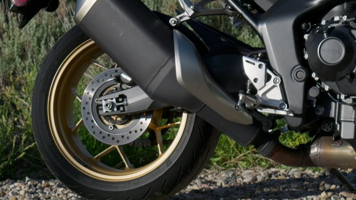 Close detail of the Honda CB1000 Hornet SP's large muffler and gold rear wheel
