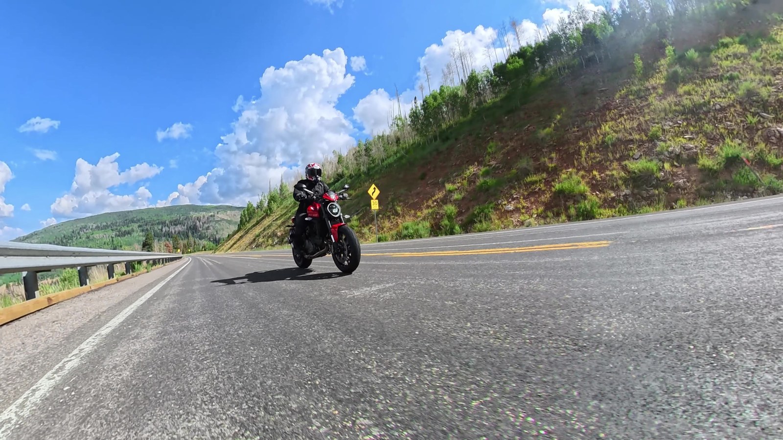 A red Ducati Monster being ridden on a sunny canyon road