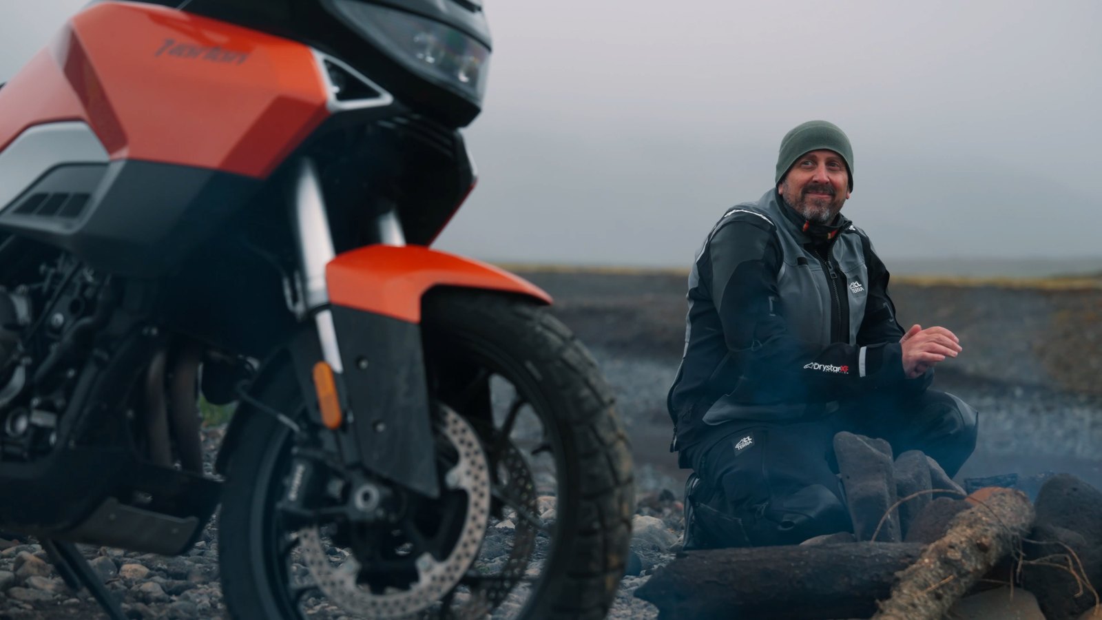 Dave sitting beside a fire on a black-sand Icelandic beach next to the Norton Atlas