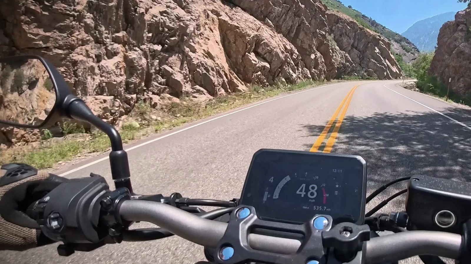 Point-of-view riding shot down a canyon road showing a Triumph dash and handlebars