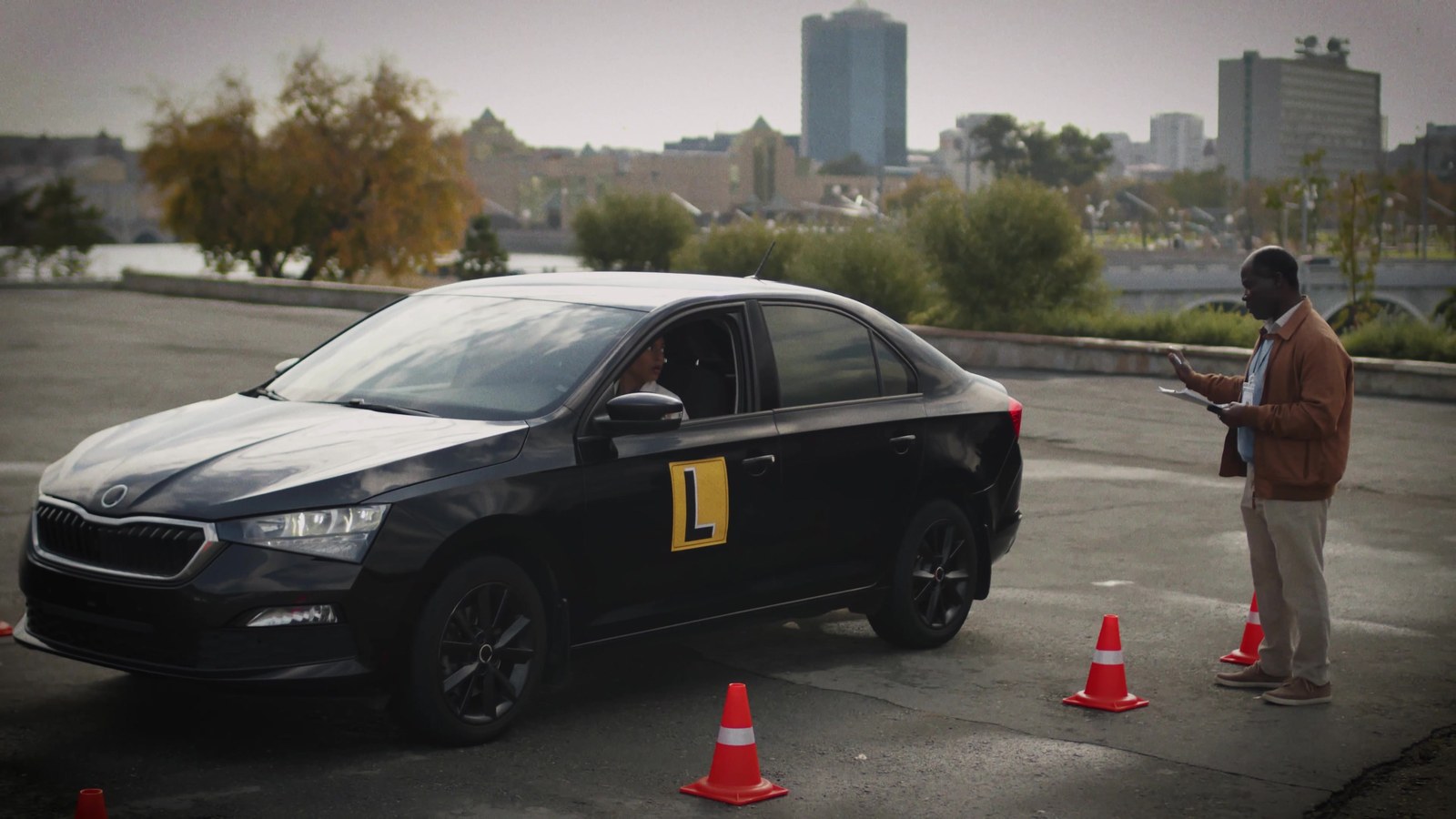A learner driver in a driving-school car with traffic cones and an instructor holding a clipboard