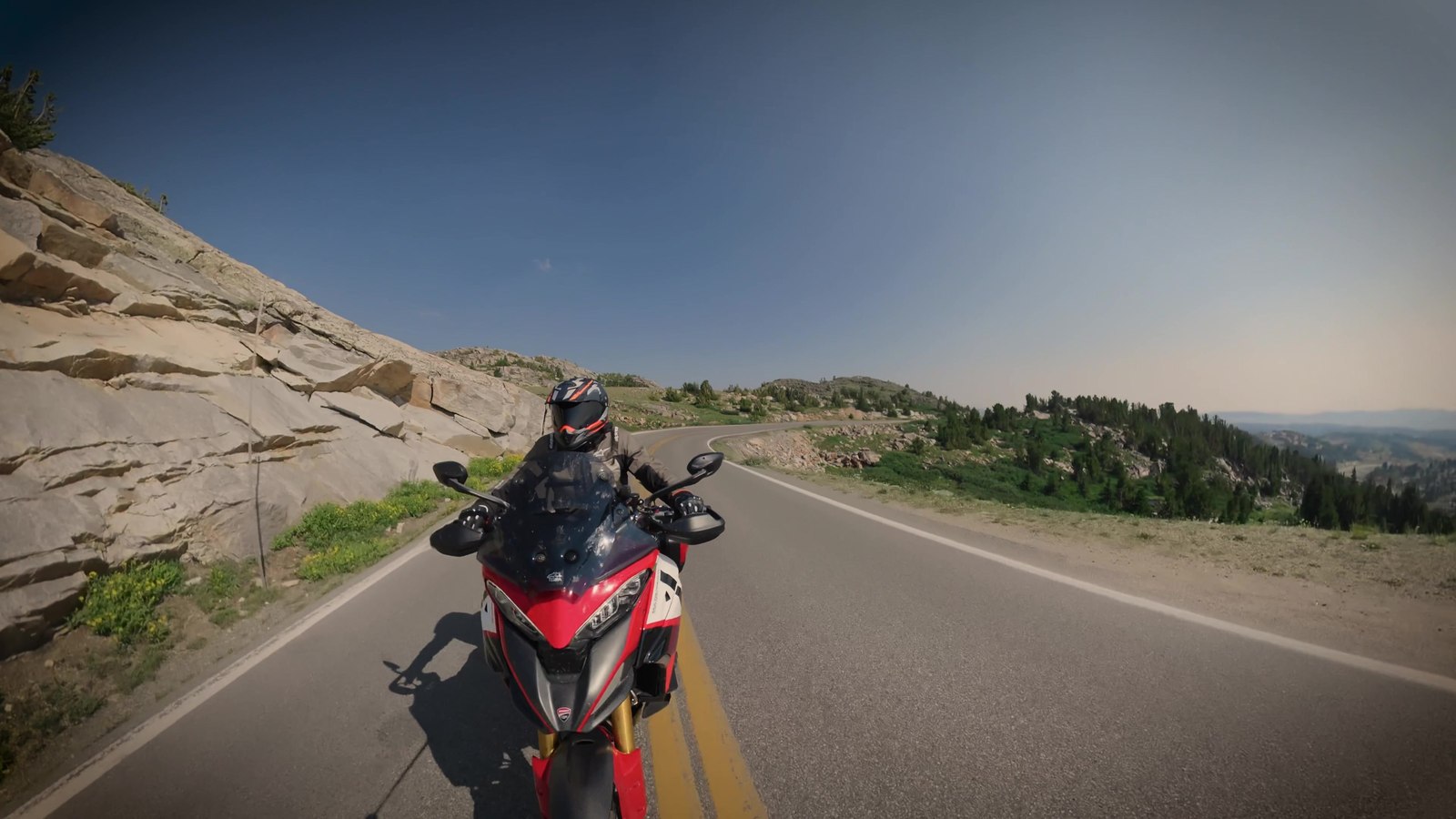 A red Ducati Multistrada riding toward the camera on a sunlit mountain road