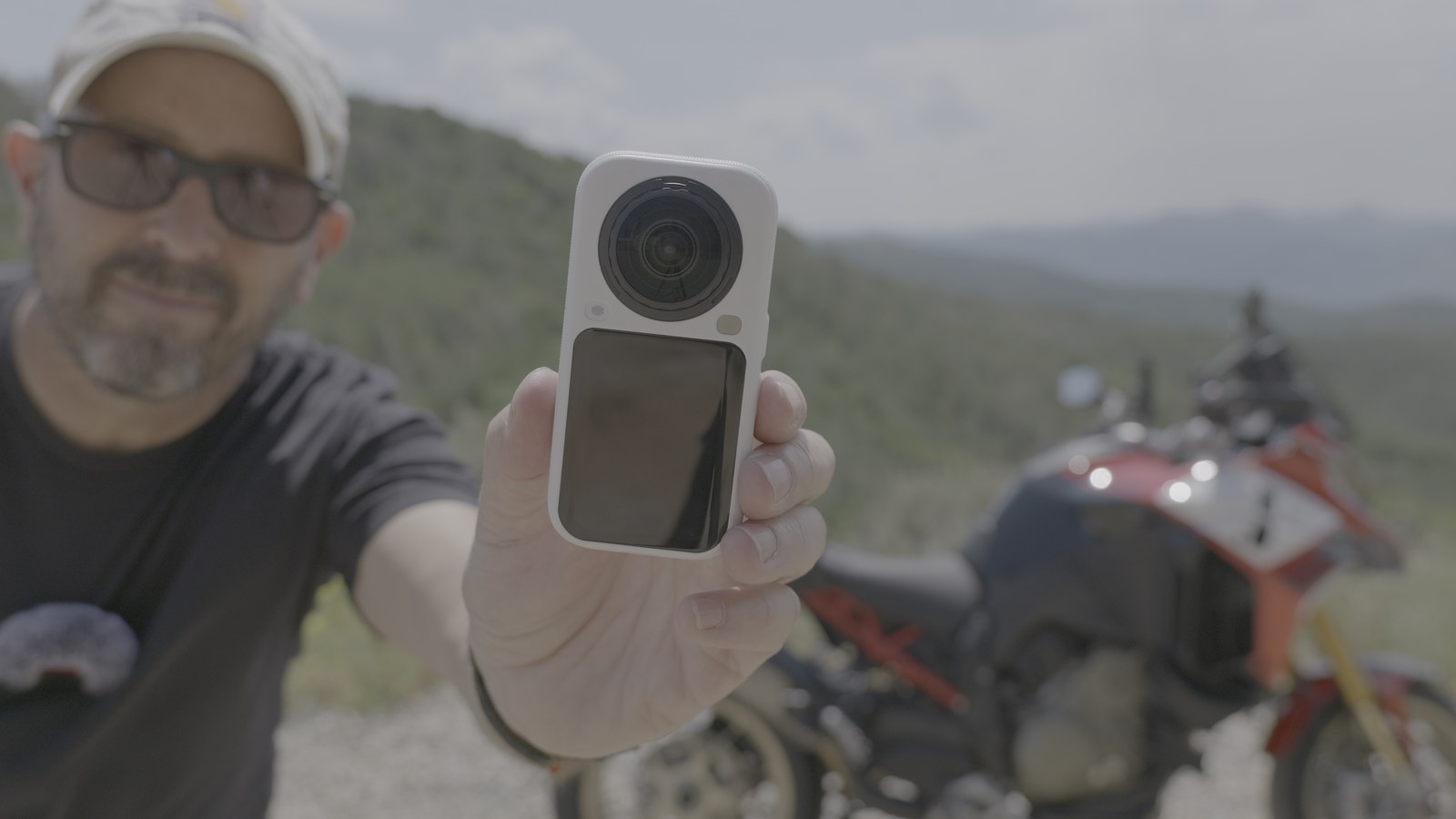 Hand holding the white Insta360 X6 camera up to the lens with a motorcycle blurred behind