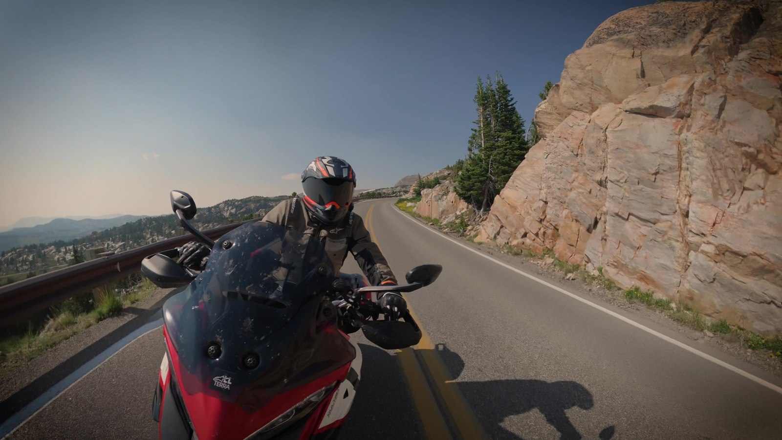 A rider on a red Ducati Multistrada on a mountain road, filmed from a floating third-person chase angle