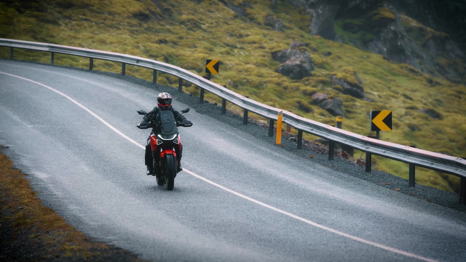 A red Norton Atlas adventure bike riding toward camera on a misty, wet mountain road in Iceland