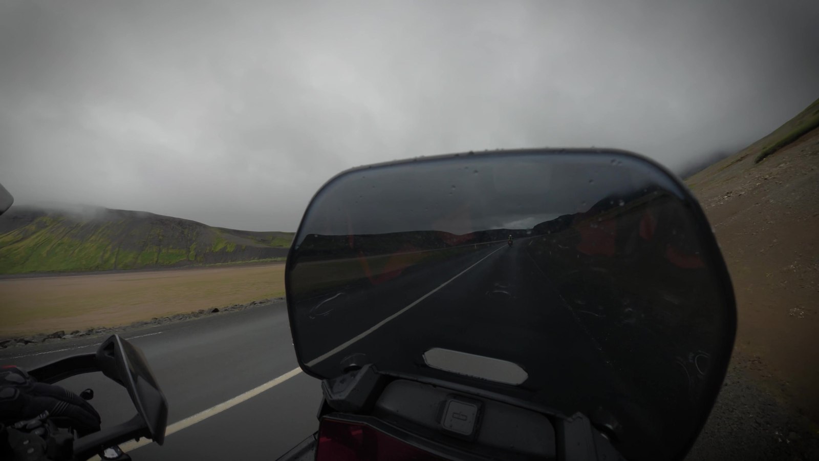 POV over a motorcycle windscreen on a mountain road under a dark, stormy sky