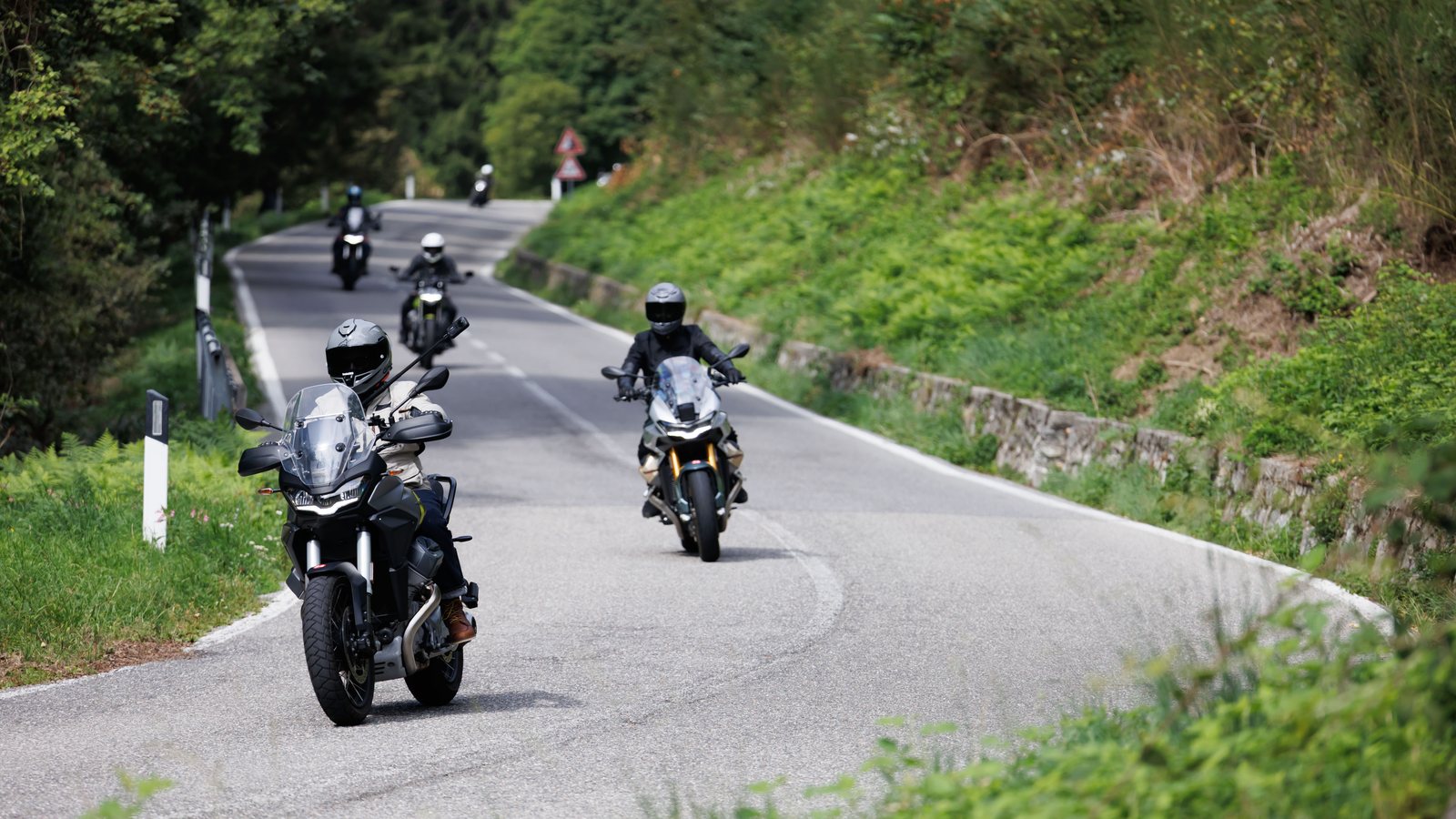 A group of riders on Moto Guzzis on a mountain road above Lake Como
